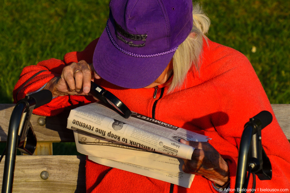 Senior reader with loupe at English Bay shore in Vancouver West End 